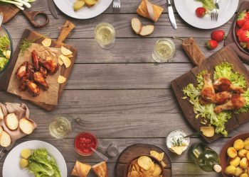 Outdoors Food Concept. On the wooden table different food with copy space grilled chicken legs buffalo wings bread salad potatoes strawberry and wine glasses with wine bottle