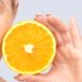 portrait of young woman with eyes closed holding orange and showing and promoting a healthy eating and a healty lifestyle.