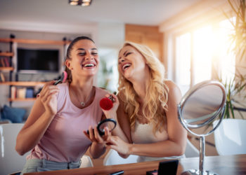 Two happy girls applying make up at home,having fun together.