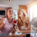 Two happy girls applying make up at home,having fun together.